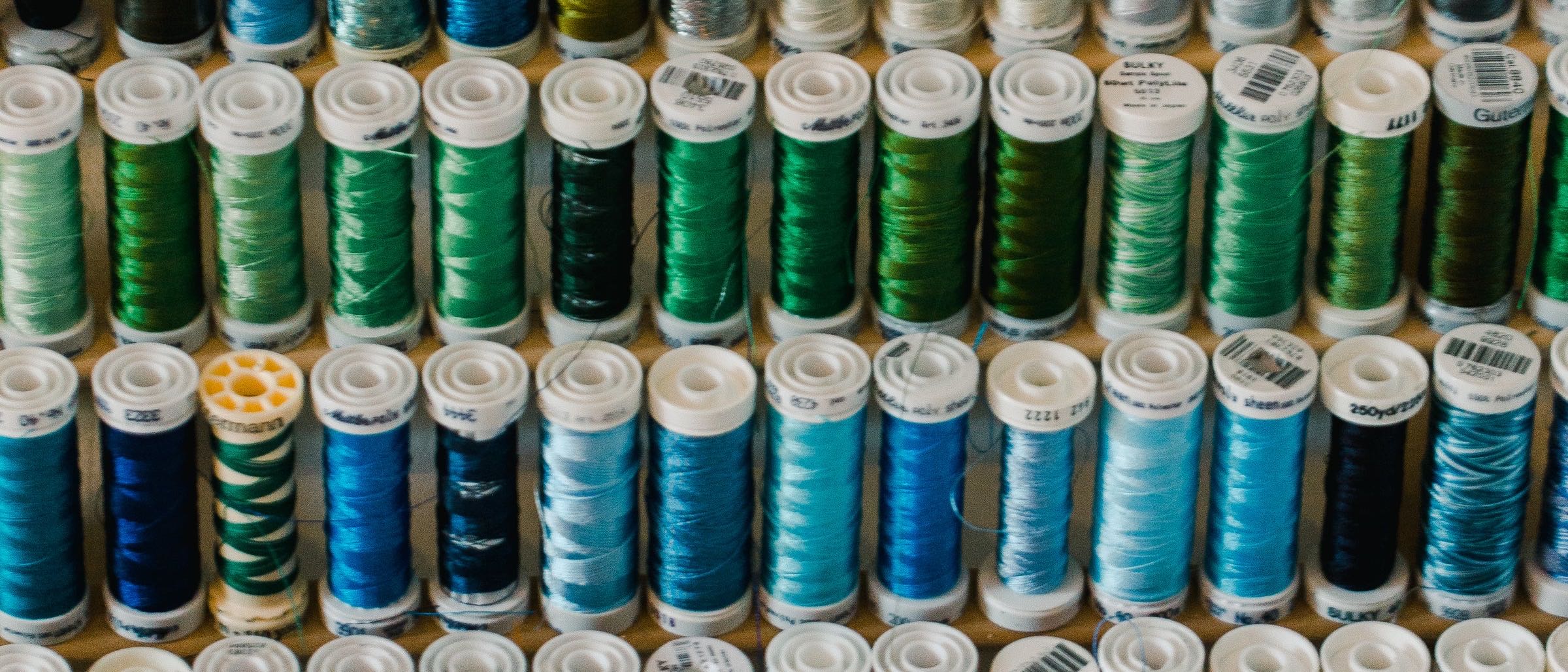 Spools of blue and green thread stacked on a shelf